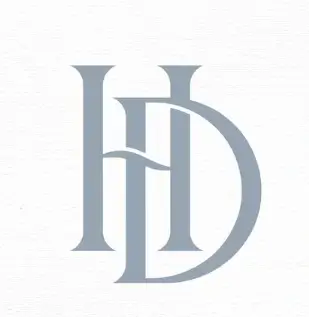 A kitten sits patiently between a terracotta pot and decorative grasses.